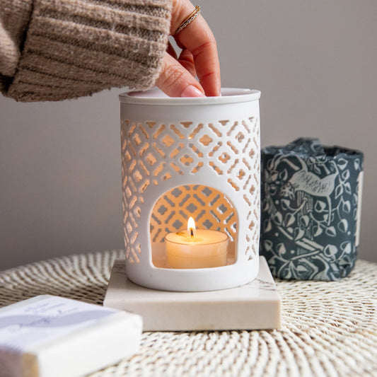 Placing Elsie and Tom wax melts into a ceramic oil burner that is lit with a soya tea light and a relaxing embrace wrapped candle in the background.